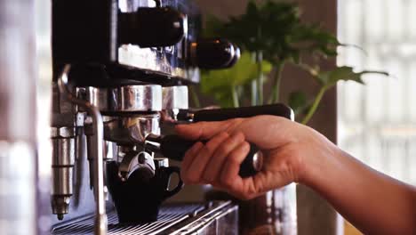 Waitress-using-a-tamper-to-press-ground-coffee-into-a-portafilter