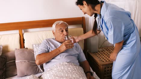 Nurse-giving-a-glass-of-water-to-senior-man-in-bedroom