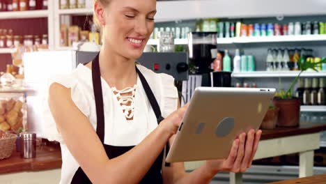 Smiling-waitress-standing-at-counter-using-digital-tablet