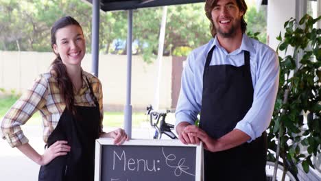Waiter-and-waitress-standing-with-menu-board-outside-the-cafe