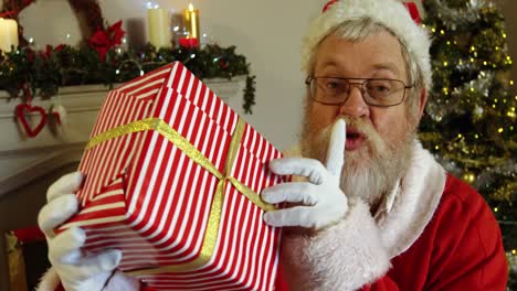 Porträt-Des-Weihnachtsmanns,-Der-Eine-Geschenkbox-Mit-Dem-Finger-Auf-Den-Lippen-Hält