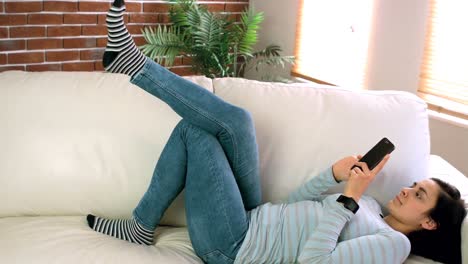 Woman-using-mobile-phone-while-lying-on-couch-in-living-room
