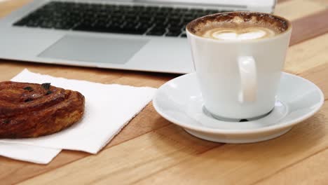 Close-up-of-laptop-with-coffee-cup-and-sweet-cookie