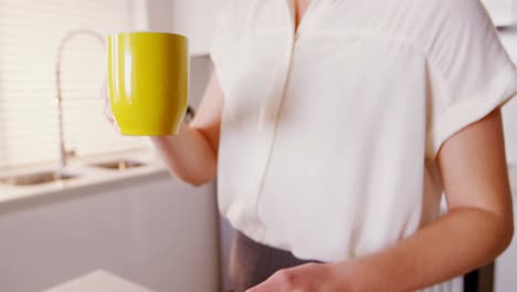 Frau-Benutzt-Mobiltelefon-Und-Laptop,-Während-Sie-In-Der-Küche-Kaffee-Trinkt