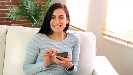 Woman-sitting-on-couch-using-mobile-phone-in-living-room