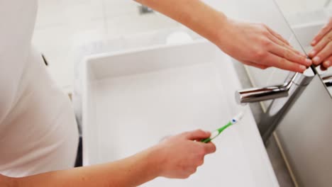Woman-washing-toothbrush-under-sink-in-bathroom