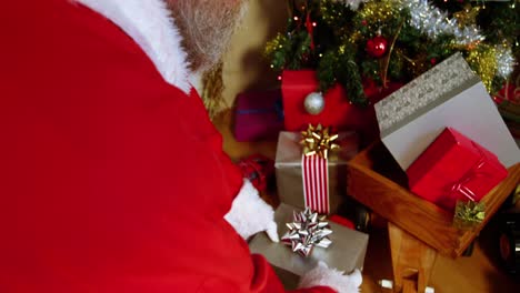 Santa-claus-placing-gift-box-near-christmas-tree