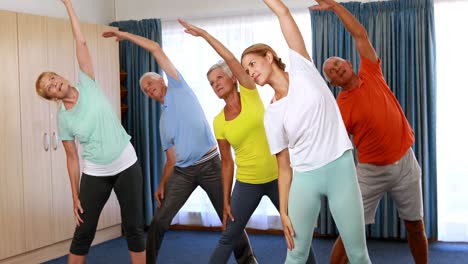Trainer-assisting-senior-citizens-in-performing-stretching-exercise