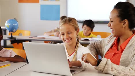 Teacher-and-schoolgirl-using-laptop-in-classroom