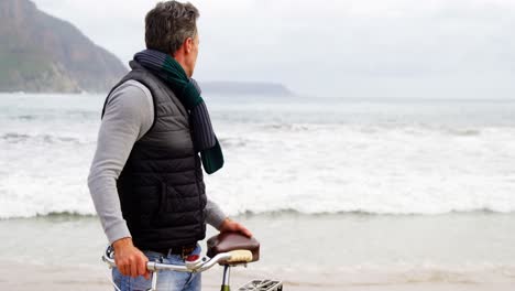 Man-standing-with-her-bicycle-on-beach