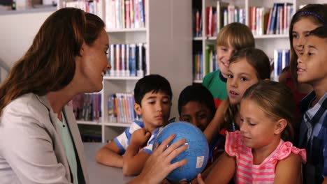Teacher-assisting-school-kids-in-reading-globe-in-library