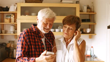 Senior-couple-listening-music-on-smartphone-in-kitchen