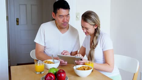 Happy-couple-using-digital-tablet-while-having-breakfast