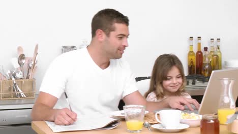Father-working-with-a-laptop-in-the-kitchen-and-daughter-having-breakfast