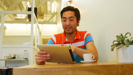 Man-using-digital-tablet-while-having-coffee-cup-on-table