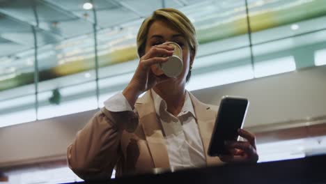 Businesswoman-holding-mobile-phone-and-drinking-coffee