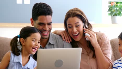 Happy-family-using-laptop,-mobile-phone,-digital-tablet-in-living-room