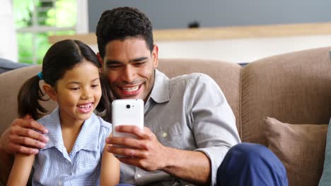 Father-and-daughter-using-mobile-phone-in-living-room