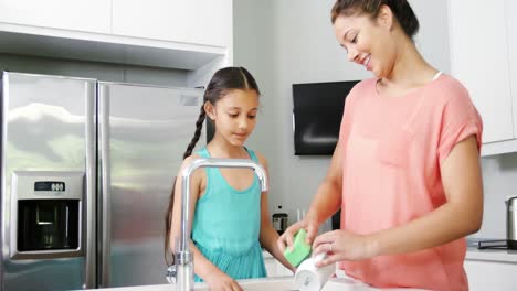 Mother-teaching-daughter-to-washing-crockery-in-kitchen