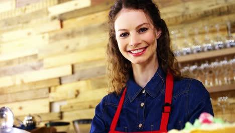 Portrait-of-smiling-waitress-holding-cake-at-counter