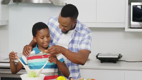 Father-and-son-preparing-vegetable-salad-in-kitchen