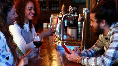 Barman-taking-order-from-female-customers-at-bar-counter