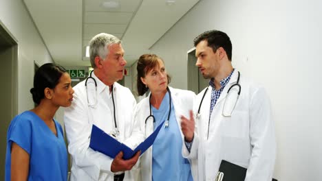 Doctors-and-nurse-discussing-over-medical-report-while-walking-in-corridor