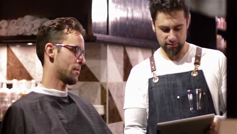 Male-barber-showing-digital-tablet-to-customer