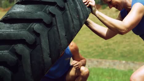 Woman-performing-workout-with-tire-at-boot-camp