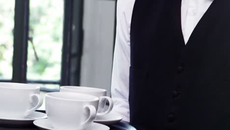 Mid-section-of-waiter-holding-a-tray-of-coffee-cups