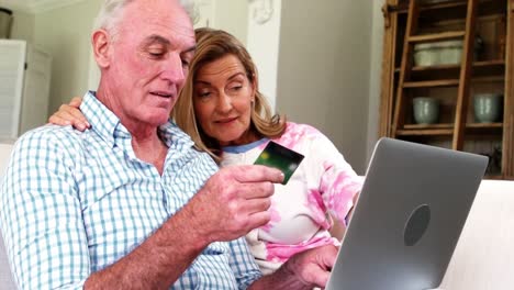 Smiling-senior-couple-doing-online-shopping-on-laptop-in-living-room