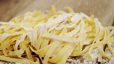 Close-up-of-flour-springing-on-uncooked-tagliatelle-pasta-on-wooden-background