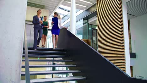 Businesswomen-interacting-with-each-other-while-walking-on-stairs