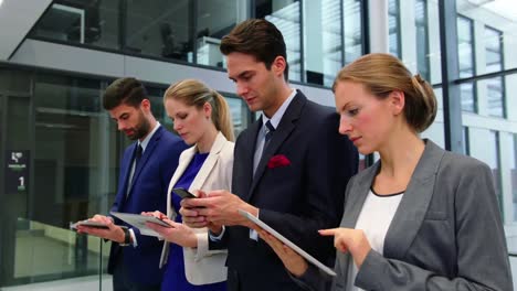 Business-executives-using-mobile-phone-and-digital-tablet-in-corridor