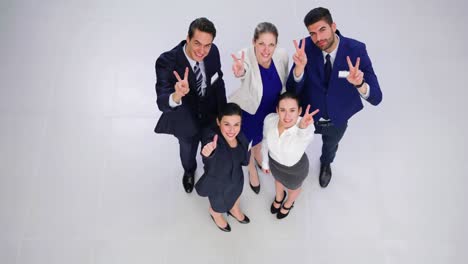 Smiling-businesspeople-showing-thumbs-up-and-peace-hand-sign-in-office