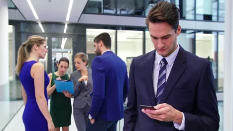 Businessman-using-mobile-phone-and-colleague-discussing-in-background