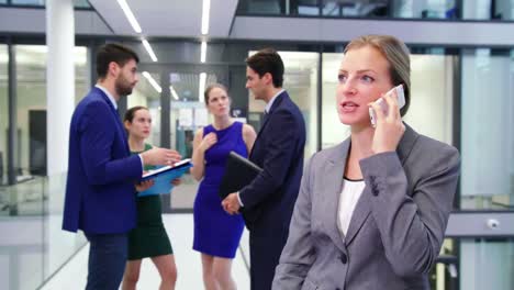 Businesswoman-talking-on-mobile-phone-while-businesspeople-discussing-in-background