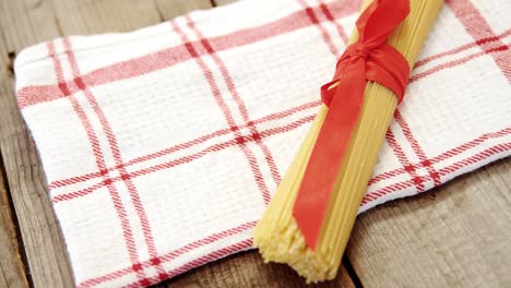 Bunch-of-raw-spaghetti-tied-up-with-red-ribbon-on-red-and-white-napkin-on-wooden-background