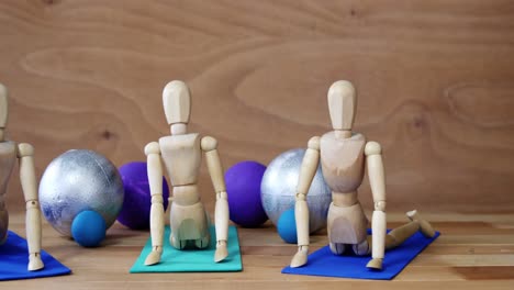 Wooden-figurine-exercising-on-exercise-mat-in-front-of-gym-balls-against-wooden-background