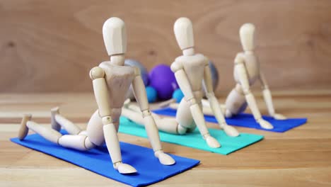 Wooden-figurine-exercising-on-exercise-mat-in-front-of-gym-balls-against-wooden-background