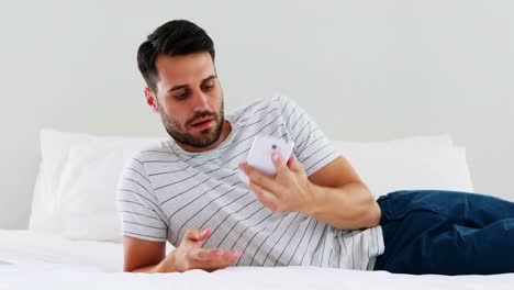 Man-using-mobile-phone-on-bed-in-bedroom