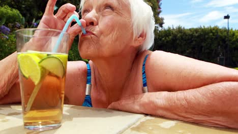 Ältere-Frau-Trinkt-Ein-Glas-Eistee-Im-Pool