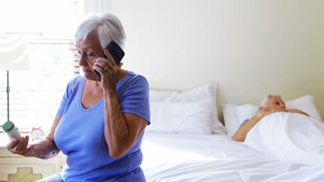 Ältere-Frau,-Die-Mit-Dem-Mobiltelefon-Spricht-Und-Eine-Medikamententablette-In-Der-Hand-Hält