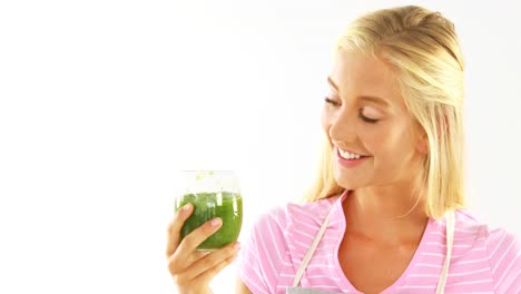 Smiling-woman-drinking-vegetable-smoothie-against-white-background