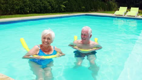 Senior-couple-swimming-in-the-pool-with-inflatable-tubes