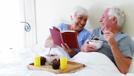 Senior-couple-interacting-with-each-other-while-having-breakfast-on-bed