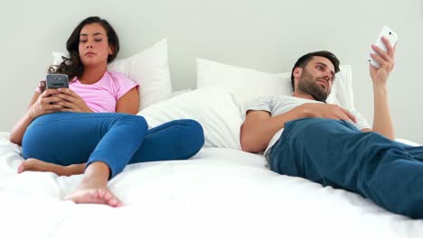 Couple-using-mobile-phone-on-bed-in-the-bedroom
