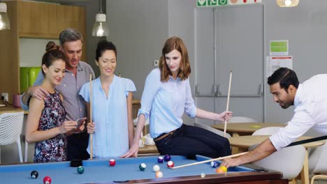 Executive-taking-picture-with-mobile-phone-while-colleagues-playing-pool