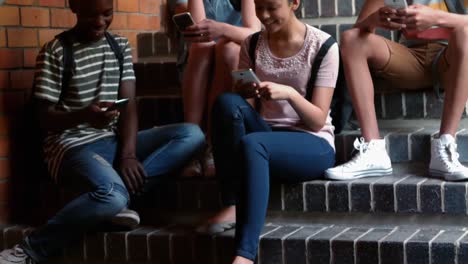 Classmates-sitting-on-staircase-and-using-mobile-phone
