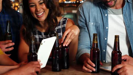 Smiling-group-of-friends-using-digital-tablet-while-having-bottle-of-beer